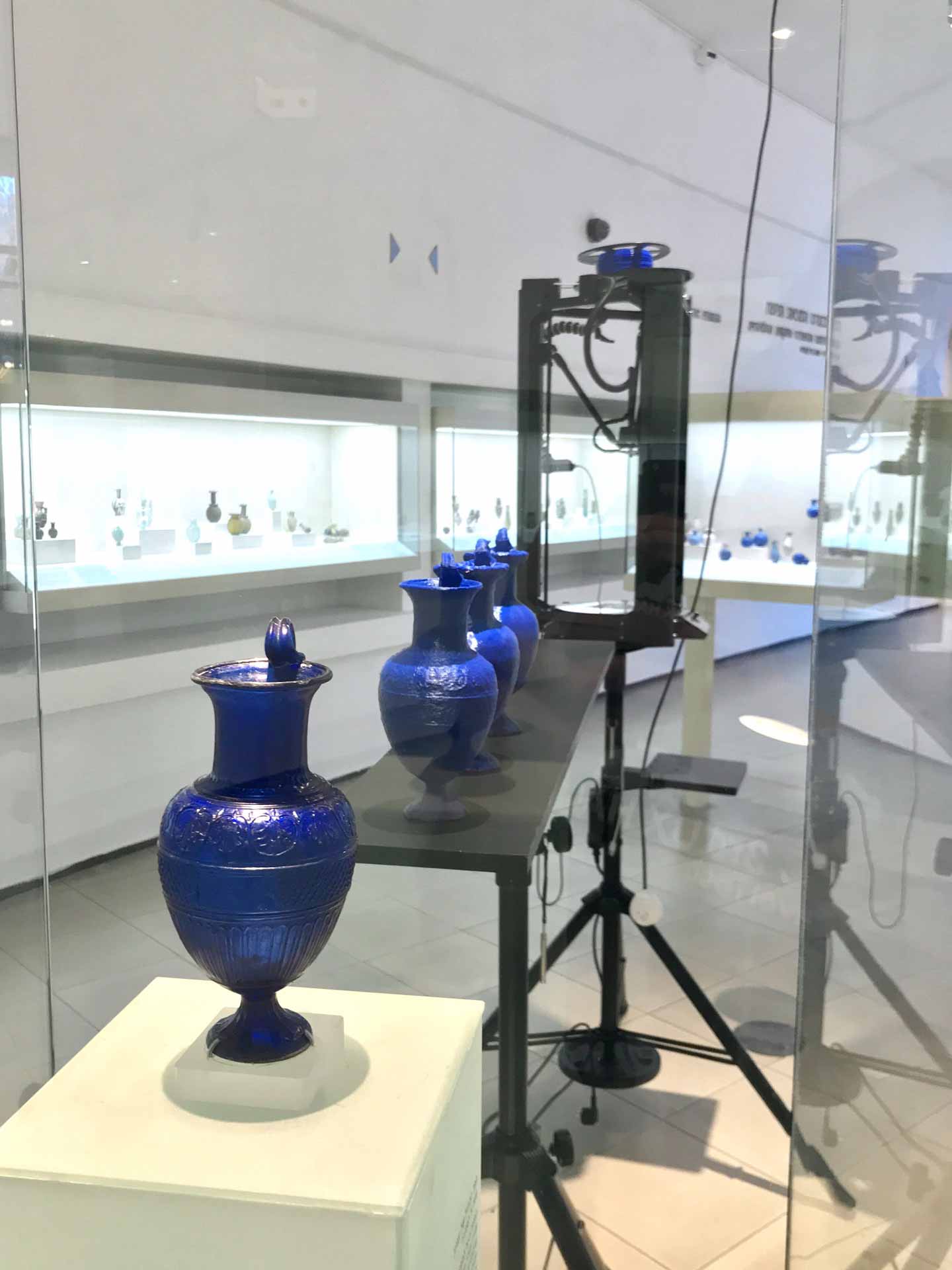 A museum display showing the original blue jug in a vitrine, beside which there are four 3D-printed jug replicas and a 3D printer.