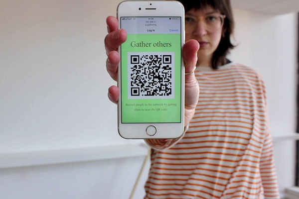 A woman holding a phone to the camera bearing a QR code and the words "gather others".
